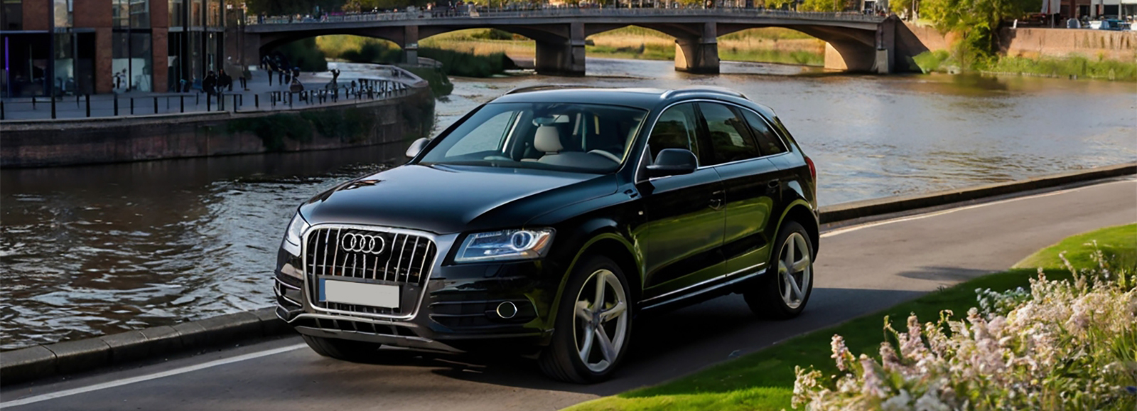 A Black Luxury Audi SUV is driving down a street next to a river